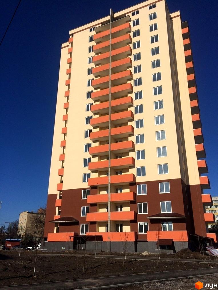 Багатоповерховий будинок Житлового комплексу Рось з бежевим та коричневим фасадом, помаранчевими балконами. На передньому плані видно ґрунт та молоді дерева.