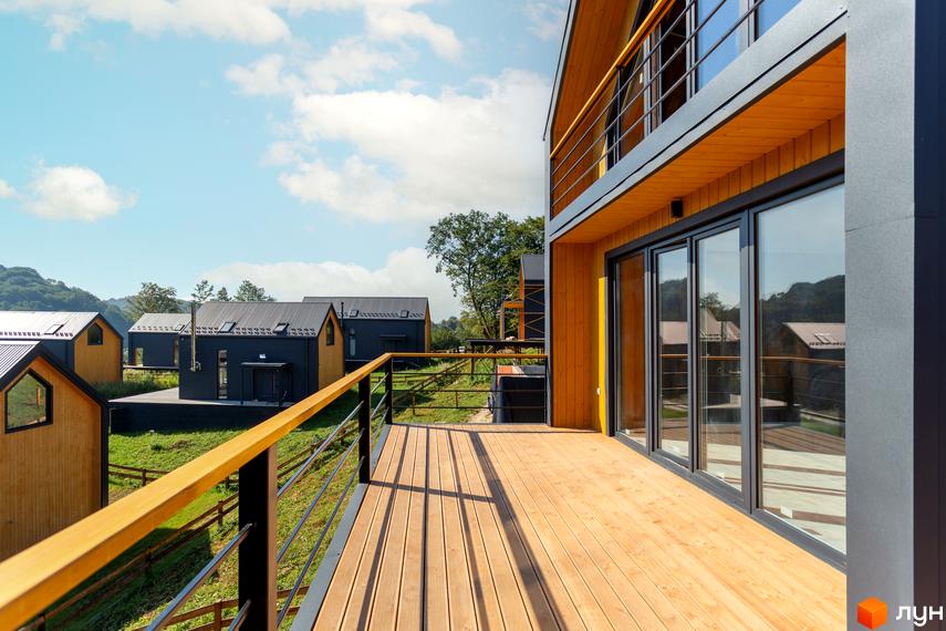 Котеджне містечко Схили: дерев'яні фасади будинків з чорними дахами та великими вікнами, зелена територія з терасами та огорожею.