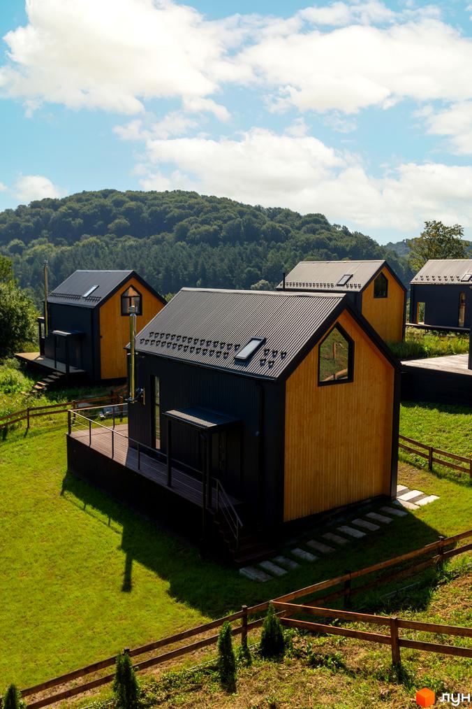 Котеджне містечко Схили: сучасні дерев'яні будинки з чорними дахами та прибудинковою територією з газоном та дерев'яним парканом.