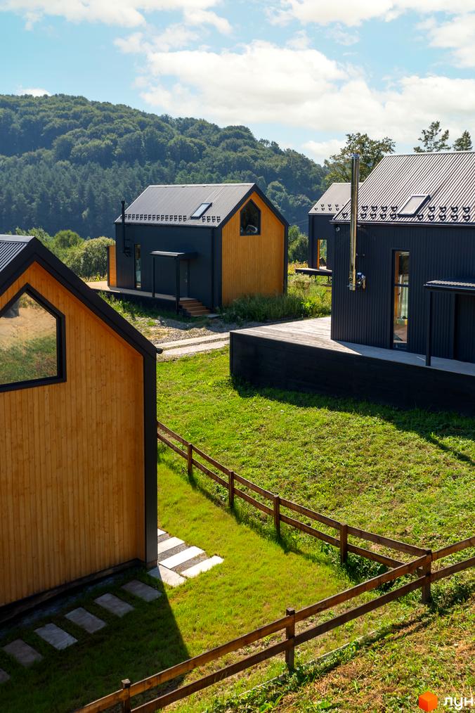 Котеджне містечко Схили: сучасні будинки з дерев'яним оздобленням на тлі зелених пагорбів та доглянута прибудинкова територія з травою та дерев'яною огорожею.