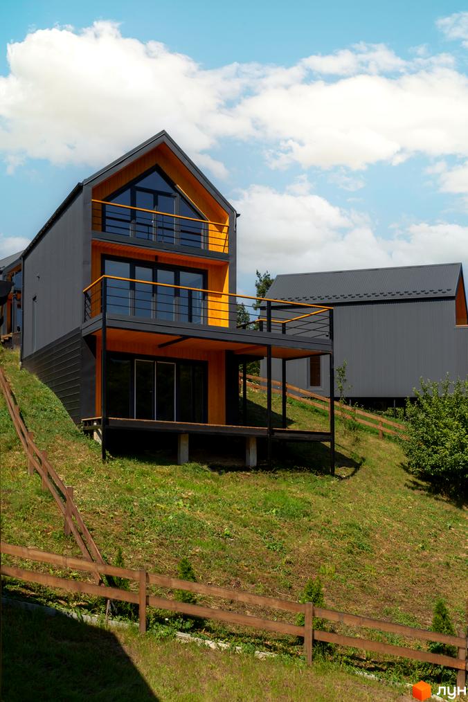 Котеджне містечко Схили має сірі фасади та жовті елементи, розташоване на схилі пагорба з дерев'яним парканом.