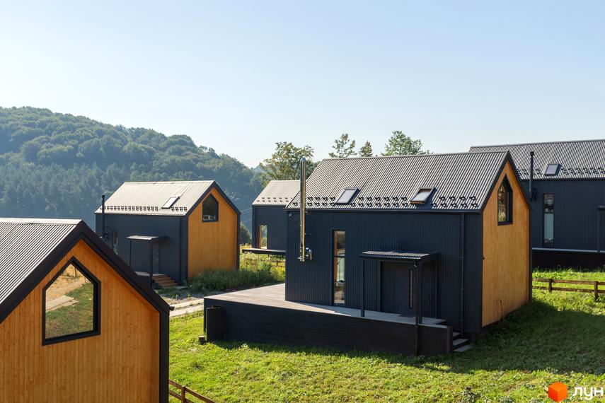 Котеджне містечко КМ Схили: сучасні будинки з дерев'яними фасадами та темними дахами на тлі зелених схилів.