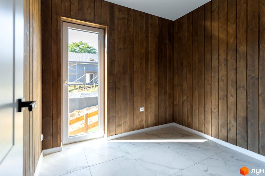 Інтер'єр кімнати з дерев'яними стінами та великим вікном, що виходить на будівництво КМ Схили. Зовнішній вигляд новобудови та прибудинкової території.