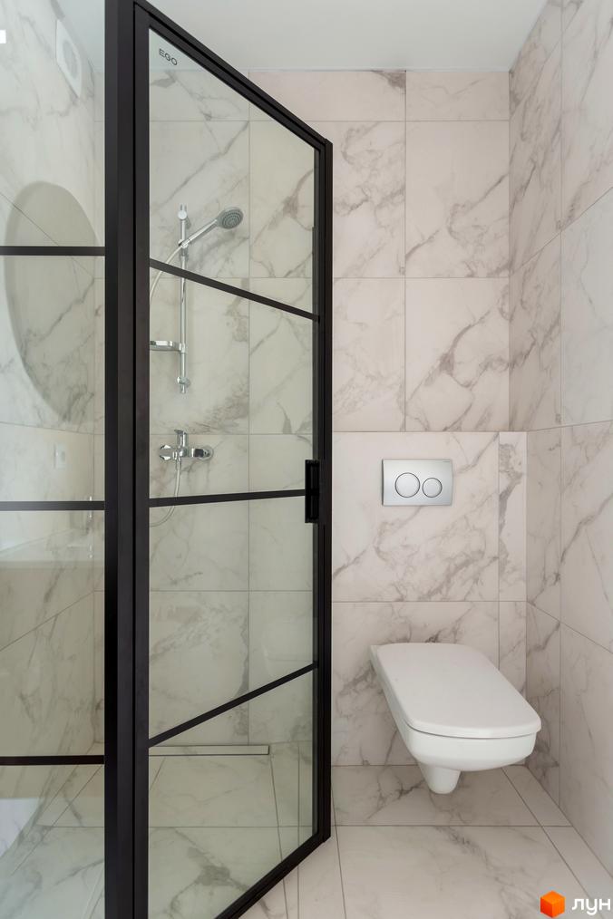 Дизайн ванної кімнати в новобудові КМ Схили з душовою кабіною та підвісним унітазом. Біла плитка з мармуровим візерунком на стінах та підлозі.