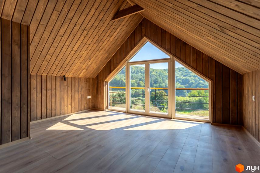 Інтер'єр мансардного поверху з панорамним вікном, що виходить на зелені схили. Відкривається вид на ліс та природу.