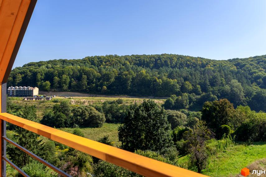 КМ Схили - житловий комплекс з фасадами з цегли та панорамними вікнами, розташований серед зелених пагорбів. Навколо комплексу - доглянута прибудинкова територія з газонами та деревами.