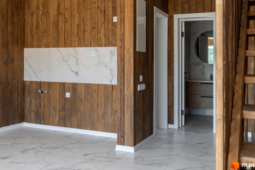 Інтер'єр будинку в житловому комплексі КМ Схили з дерев'яними стінами та мармуровою плиткою на підлозі. Відчинені двері ведуть до ванної кімнати з круглим дзеркалом.