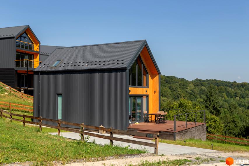 Котеджне містечко Схили: сучасні будинки з дерев'яними елементами та сірим фасадом на тлі зелених пагорбів. Прибудинкова територія з дерев'яною терасою та огорожею.