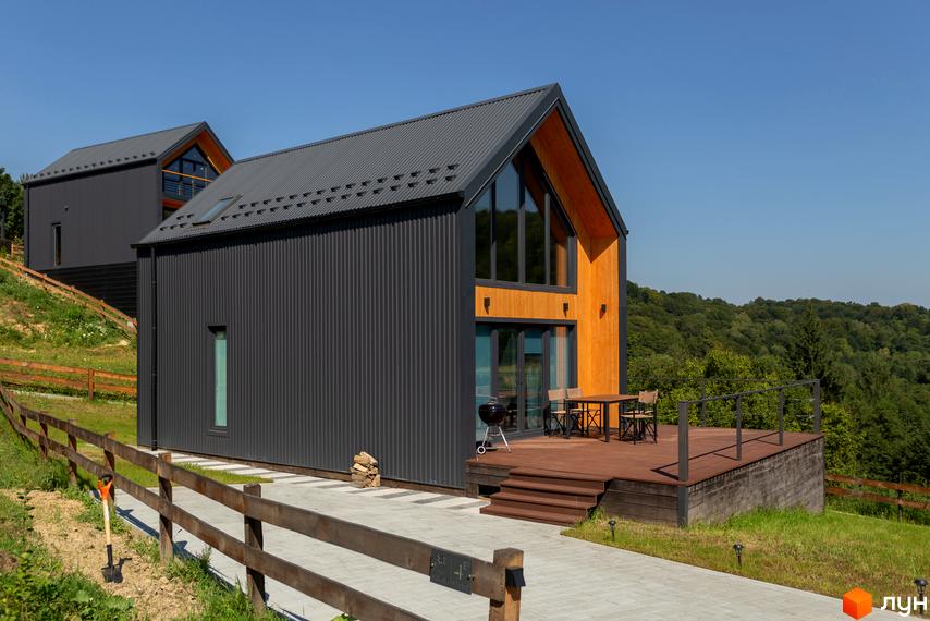 Котеджне містечко Схили: сірі будинки з дерев'яними елементами та терасою на тлі лісу. Прибудинкова територія з дерев'яним парканом та доріжкою.
