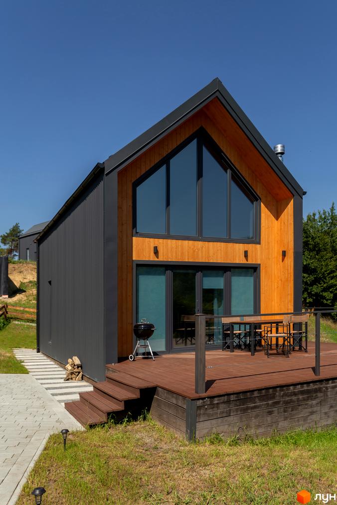 Котеджне містечко КМ Схили: двоповерховий будинок з великими вікнами та дерев'яним фасадом, терасою та зоною барбекю.