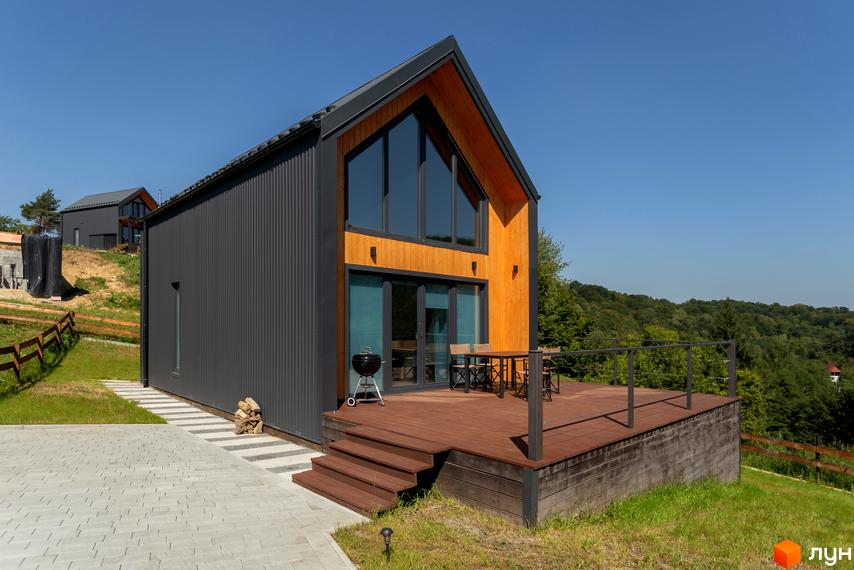 Котеджне містечко Схили: двоповерховий будинок з темним металевим фасадом, великими вікнами та дерев'яною обшивкою, з терасою та зоною для барбекю на схилі пагорба.