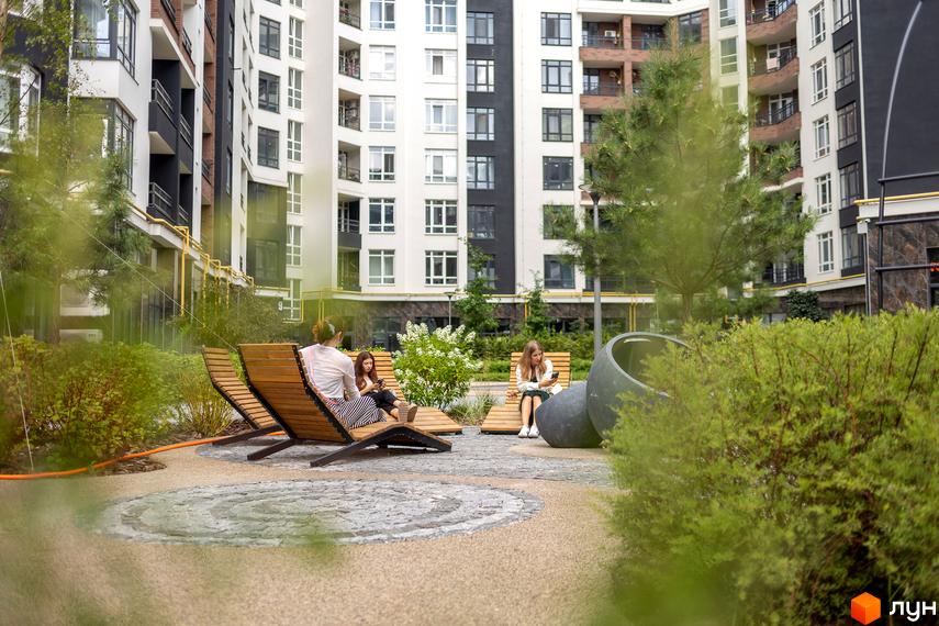 Житловий комплекс Синергія Сіті з сучасними фасадами та зоною відпочинку з дерев'яними лежаками для мешканців.