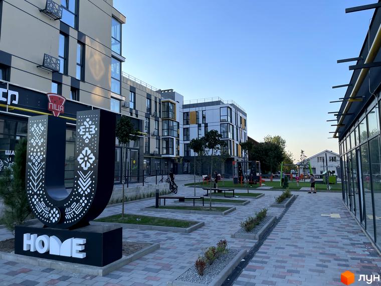 Фасади будівель Житлового комплексу U HOME світлих відтінків. Прибудинкова територія має велику декоративну літеру U з написом HOME та вимощені доріжки.
