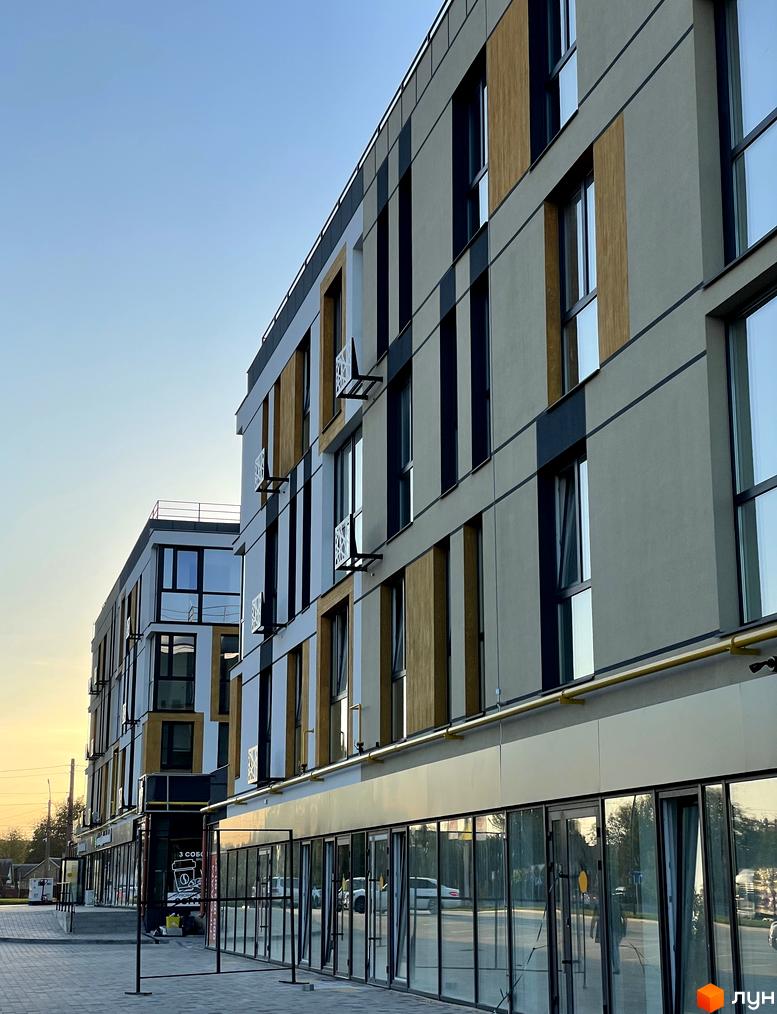 Фасад Житлового комплексу U HOME з бежевими та темними панелями, великими вікнами та комерційними приміщеннями на першому поверсі. Перед будинком бруківка.