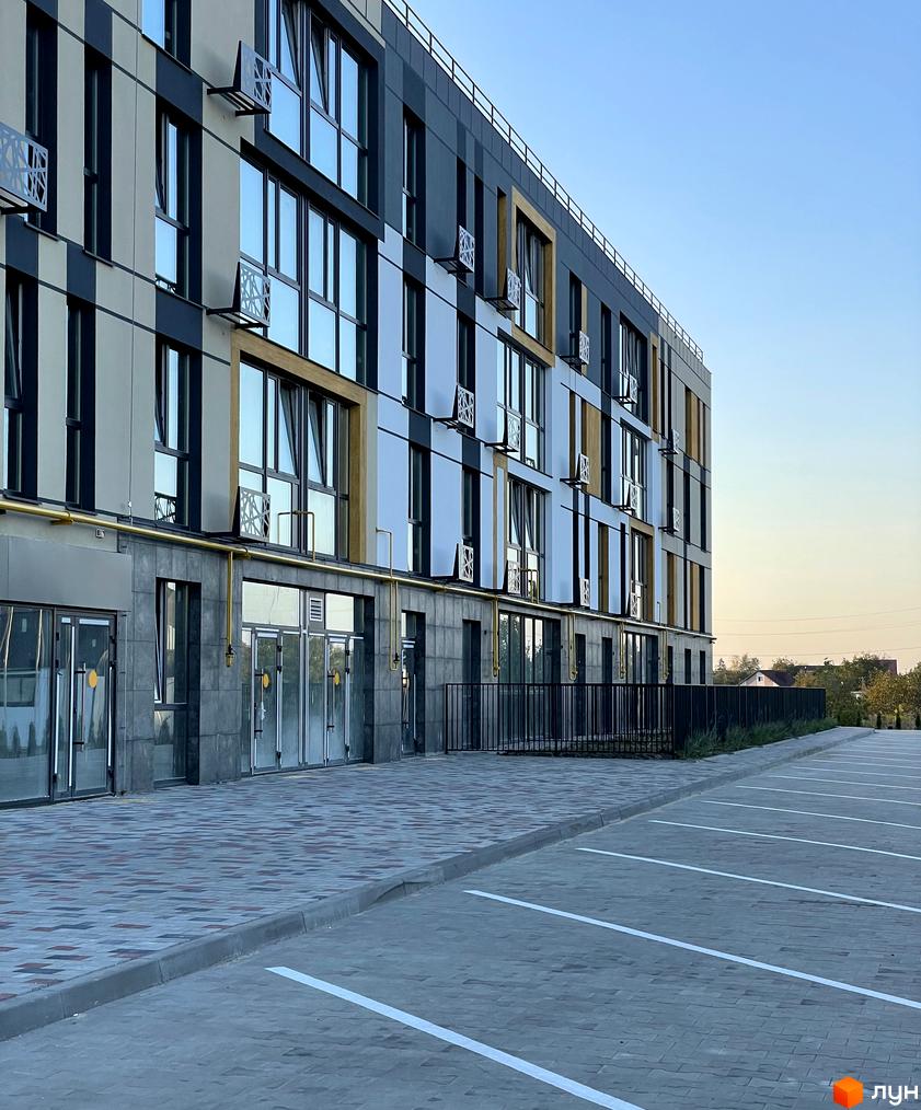 Фасад Житлового комплексу U HOME з великими вікнами та панелями різних кольорів. Поруч з будинком розташований вимощений тротуар та розмітка парковки.