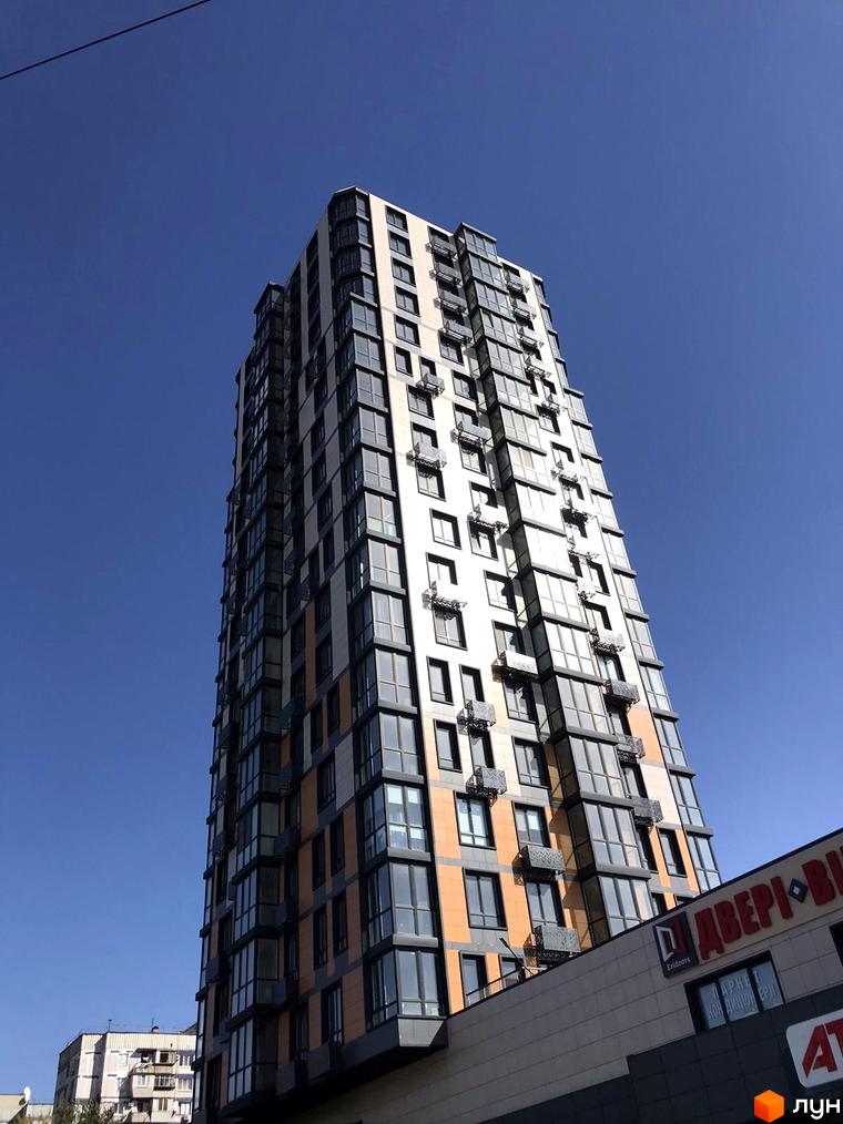 Зовнішній вигляд житлового комплексу River Hall з численними вікнами та балконами на фоні блакитного неба. На фасаді видно елементи оздоблення.