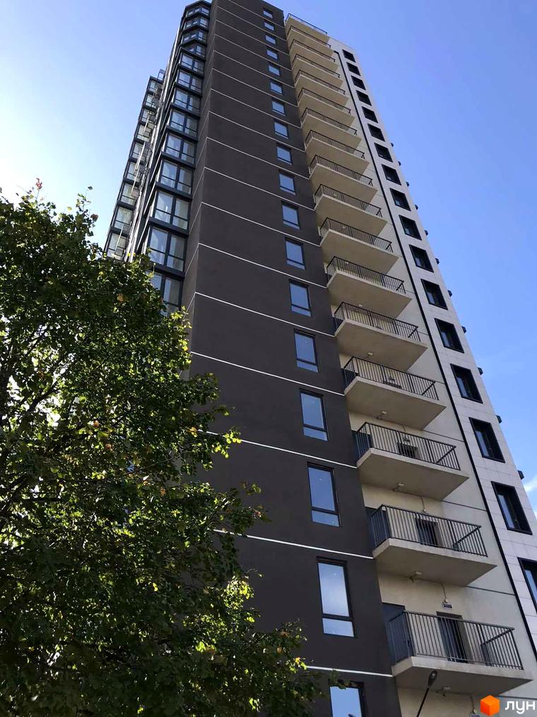 Зовнішній вигляд ЖК River Hall: висотна будівля з балконами та вікнами на тлі блакитного неба. Поруч видно зелене дерево.