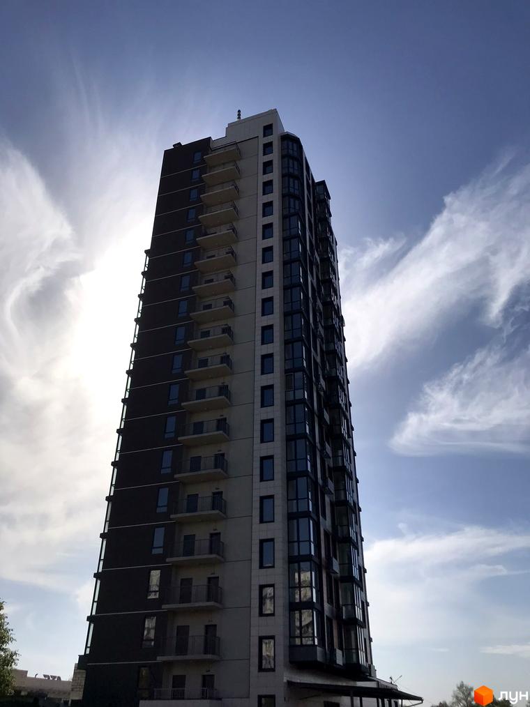 Високоповерховий житловий комплекс River Hall з балконами та скляними фасадами на тлі блакитного неба з хмарами. Зовнішній вигляд будівлі.