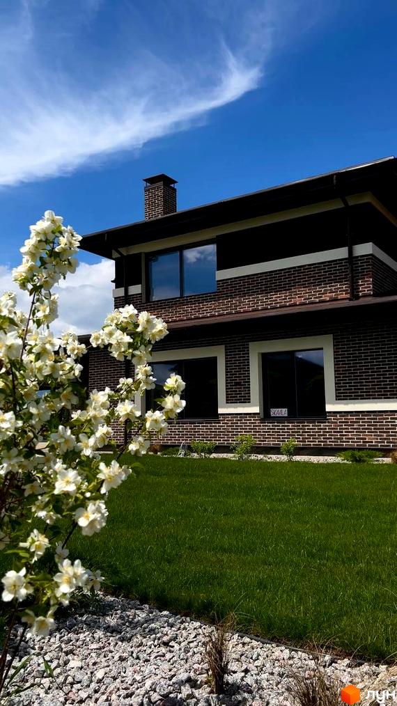 Котеджне містечко КМ Вітаград: цегляний будинок з великими вікнами та доглянутим газоном. На передньому плані квітучий кущ жасмину.