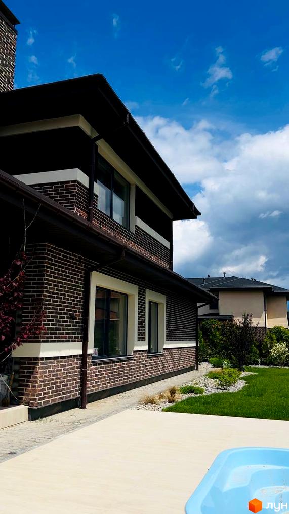 Котеджне містечко КМ Вітаград: двоповерховий будинок з цегляним фасадом та білими елементами, зелений газон та доглянута прибудинкова територія.