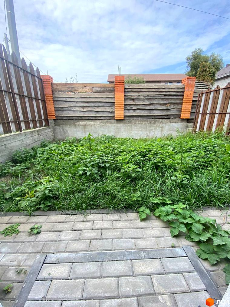 Земельна ділянка Котеджного містечка Сонячний простір з високою травою, дерев'яною огорожею та бруківкою.