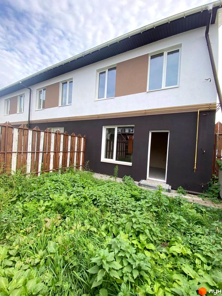 Двоповерховий будинок Котеджного містечка Сонячний простір з темно-коричневим низом та білим верхом. Перед будинком заросла зелена трава.