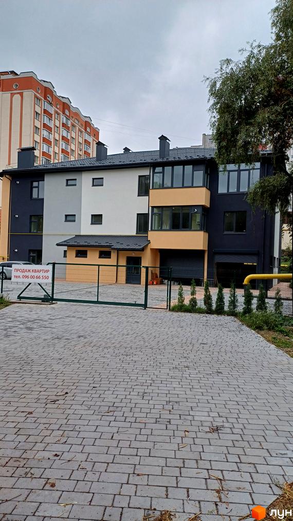 Фасад новобудови на вул. Молодіжна, 2г, з сірими та бежевими елементами, великими вікнами та огородженою територією з бруківкою.