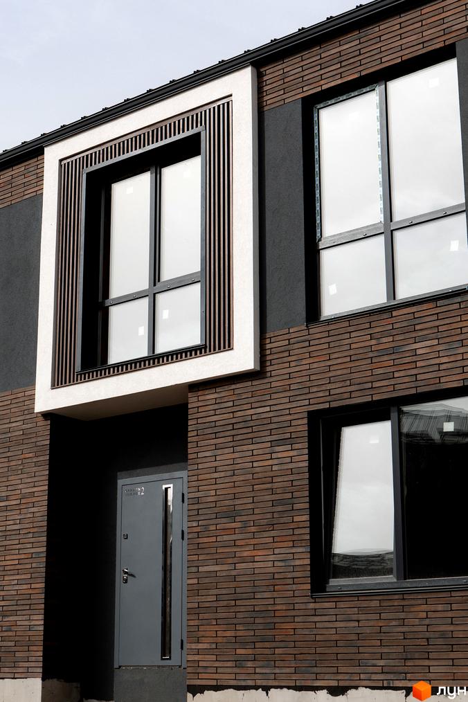 Зовнішній вигляд будинку КМ Garden Village Sofia з цегляним фасадом та великими вікнами. Сучасний дизайн фасаду з елементами дерев'яних рейок та сірими акцентами.