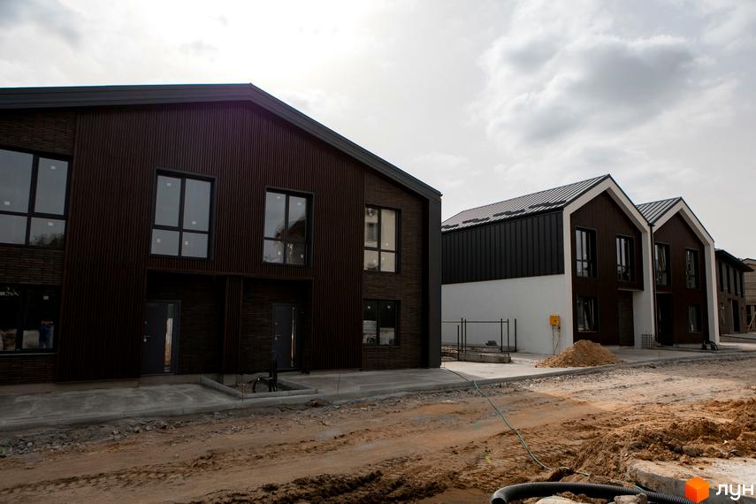 Котеджне містечко КМ Garden Village Sofia. Сучасні будинки з темним фасадом та білими елементами на тлі хмарного неба. Територія навколо будинків у стані будівництва.