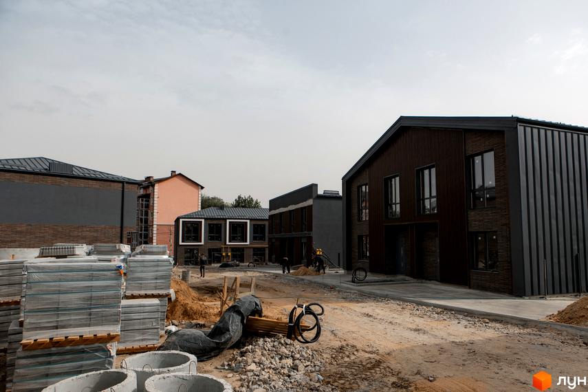 Котеджне містечко Garden Village Sofia: фасади будинків з темної цегли та металу, навколо будівельний майданчик з будматеріалами.