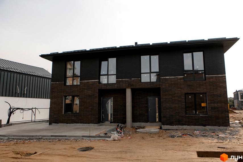 Котеджне містечко Garden Village Sofia: двоповерховий будинок з темною цегляною облицовкою нижнього поверху та чорною штукатуркою верхнього. Поруч – будівельний майданчик.