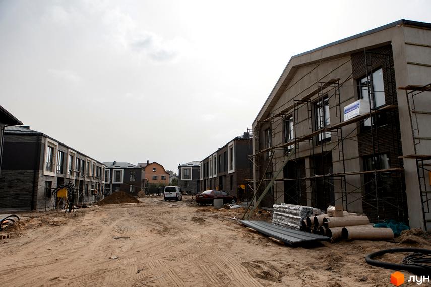 Будівельний проєкт КМ Garden Village Sofia: фасади будинків з темної цегли та штукатурки, вікна, будівельні ліси. Територія забудови з піском, трубами та будматеріалами.