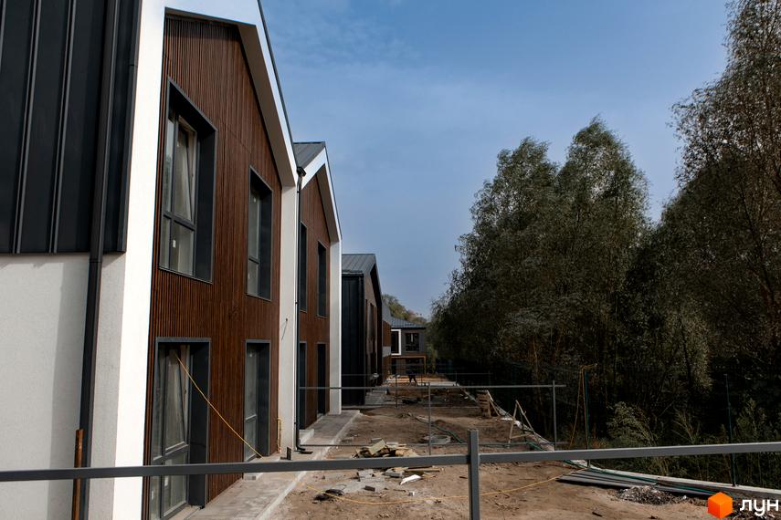 Котеджне містечко KМ Garden Village Sofia: фасади будинків з дерев'яною обшивкою та великими вікнами, прибудинкова територія з елементами будівництва.