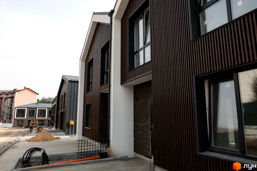 Котеджне містечко КМ Garden Village Sofia. Фасади будинків оздоблені дерев'яними рейками та цеглою, поруч будівельний майданчик з піском та комунікаціями.