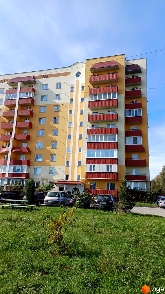 Зображення фасаду будинку по вулиці Трудова, 7/9. На передньому плані зелений газон та припарковані автомобілі.