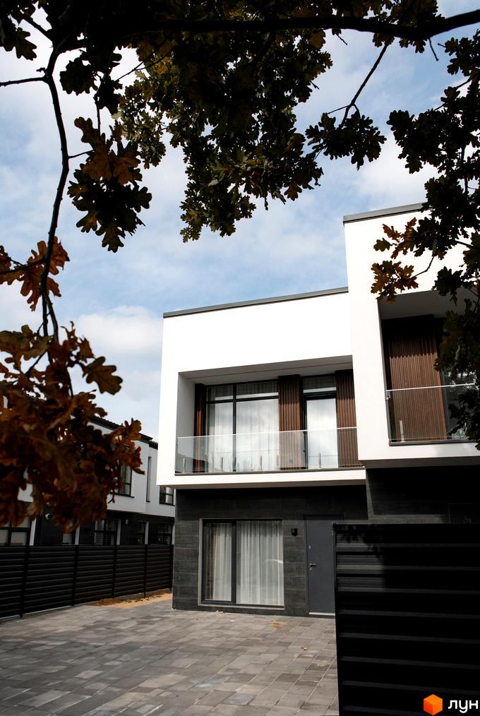 Котеджне містечко КМ Balance Homes: білі фасади з дерев'яними елементами та скляними балконами, сіра плитка на подвір'ї та чорний паркан.
