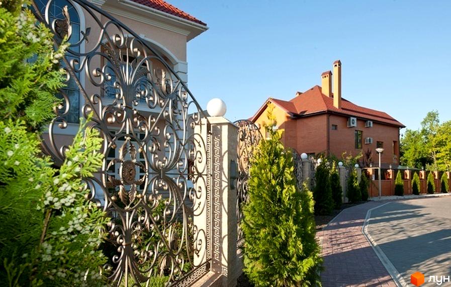 Зовнішній вигляд будинку КМ Сосновий берег з красивим парканом та зеленими насадженнями на прибудинковій території.