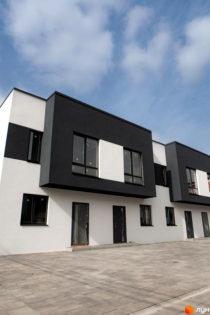 Ряд таунхаусів Таунхауси SDG Bilohorodka з чорно-білими фасадами та чорними вікнами. Прибудинкова територія викладена бруківкою.