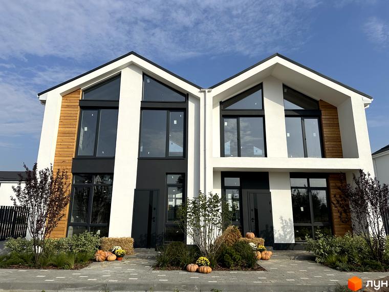 Котеджне містечко Gardd House Eco Village: дві зблоковані будівлі з білими фасадами, темними вікнами та дерев'яними елементами. Перед будинками озеленення з осіннім декором.