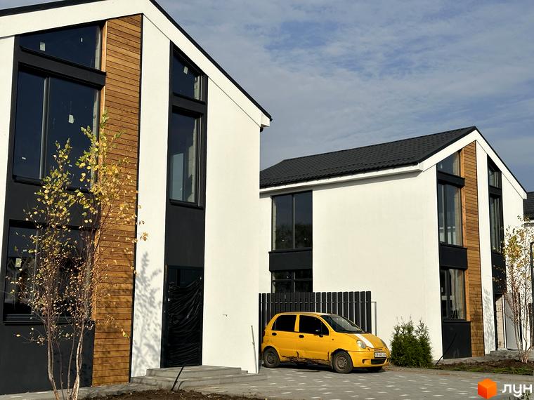 Котеджне містечко Gardd House Eco Village: білий будинок з чорними вікнами, дерев'яними панелями та прилеглою територією з жовтим авто.