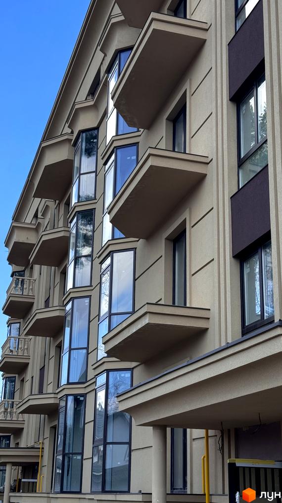 Фасад житлового комплексу Monaco з балконами та великими вікнами на тлі блакитного неба. Зовнішній вигляд будівлі з чіткими лініями та бежевим оздобленням.