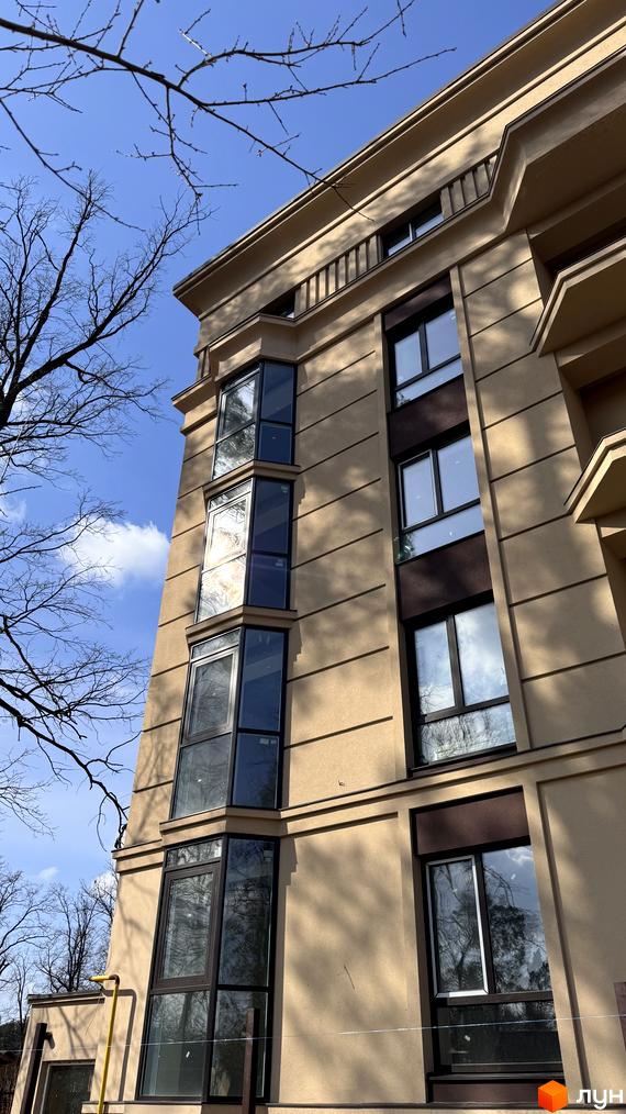 Фасад житлового комплексу Monaco з великими вікнами та балконами, що виходять на блакитне небо з хмарами. Навколо будівлі видно гілки дерев.