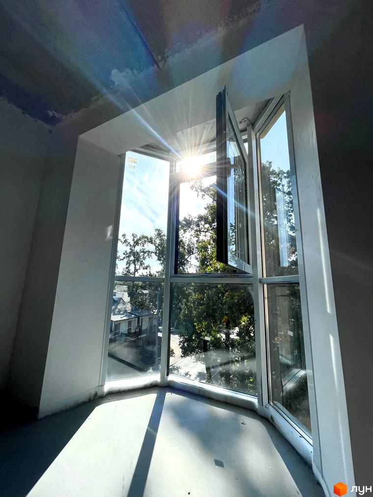 Вид з вікна на дерева та сусідні будинки в житловому комплексі Monaco. Сонячні промені проходять крізь вікно.