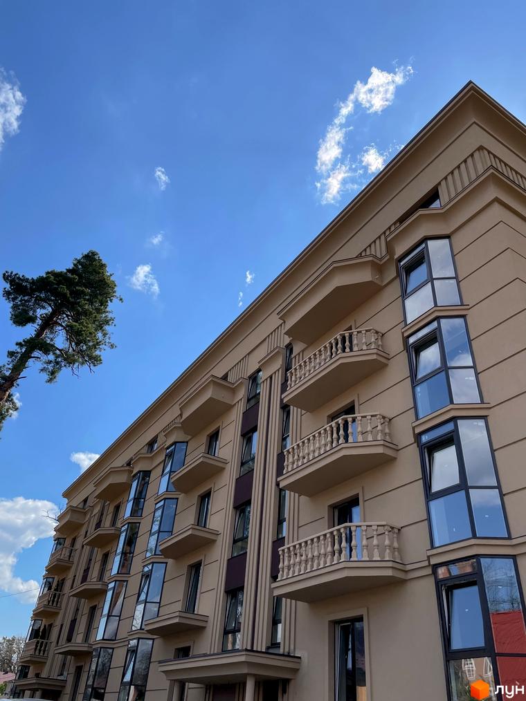 Фасад житлового комплексу Monaco з балконами та панорамними вікнами на фоні блакитного неба з хмарами. Поруч високе дерево.