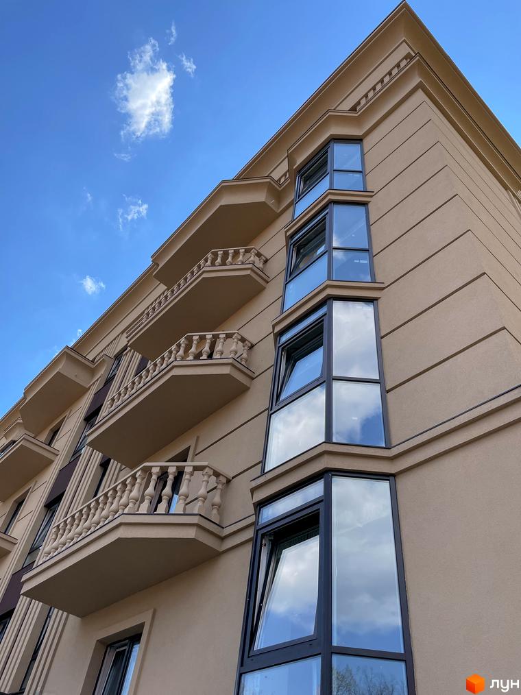 Фасад житлового комплексу Monaco з балконами та еркерними вікнами на фоні блакитного неба з хмарами. Зовнішній вигляд будівлі.