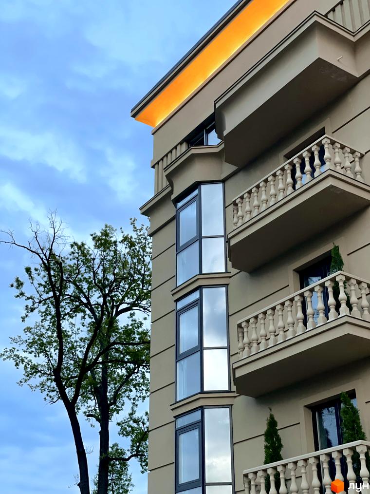 Фасад житлового комплексу Monaco з балконами та вікнами, поруч дерево на фоні неба.