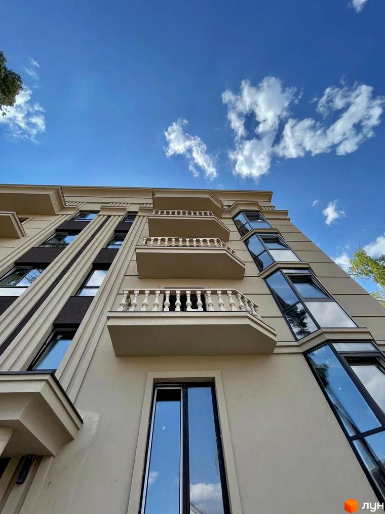 Фасад житлового комплексу ЖК Monaco з балконами та великими вікнами на тлі блакитного неба з хмарами.