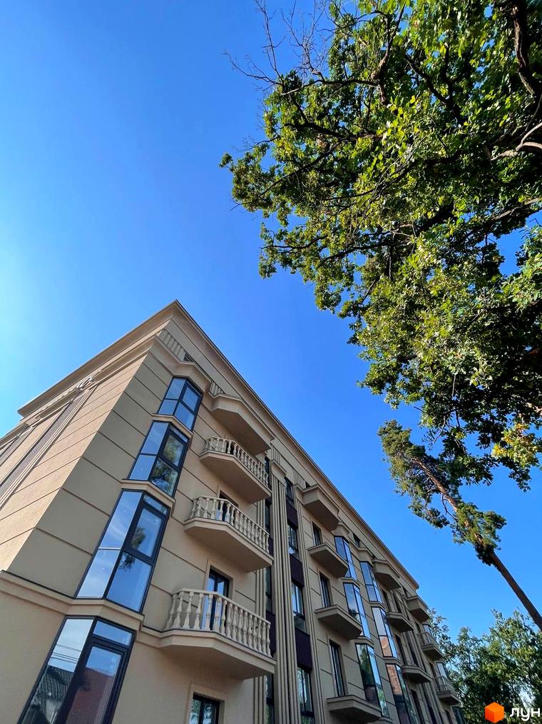Фасад житлового комплексу ЖК Monaco з балконами та великими вікнами на тлі блакитного неба та зелені дерев.