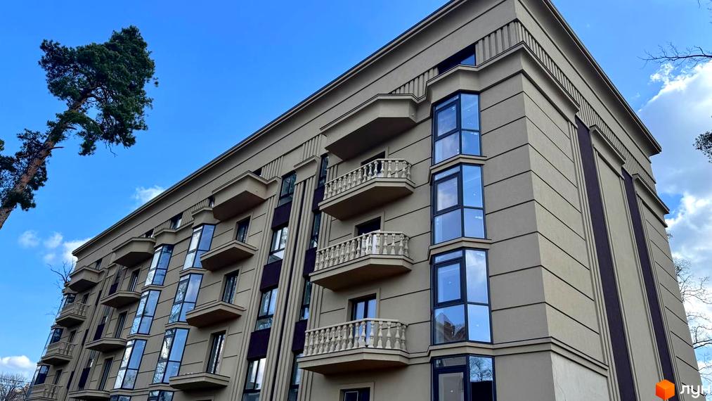 Фасад житлового комплексу Monaco з балконами та великими вікнами на тлі блакитного неба. Навколо видно дерева та зелені насадження.