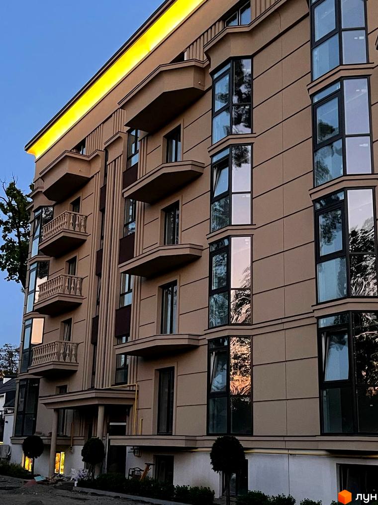 Фасад житлового комплексу Monaco з балконами та великими вікнами, що відбивають дерева та небо. Біля будинку облаштована прибудинкова територія.